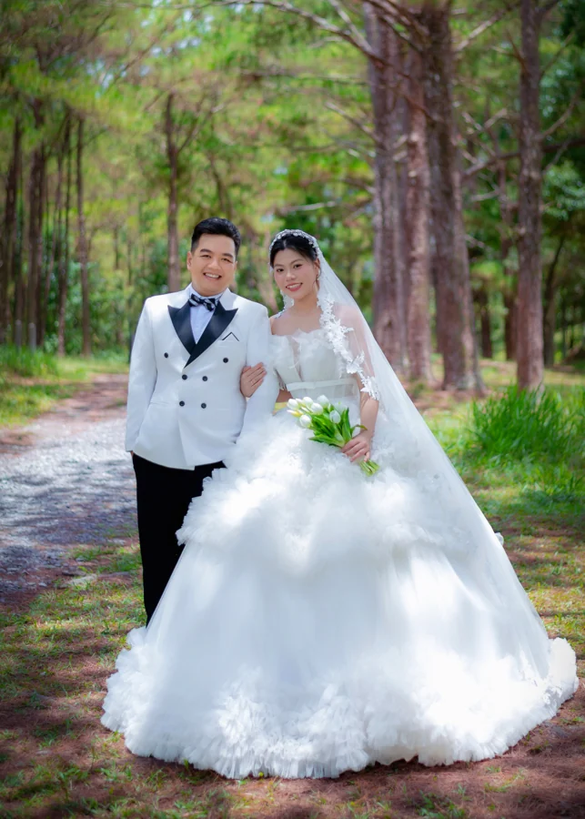 Cô dâu chú rể đứng trên lối đi giữa rừng thông